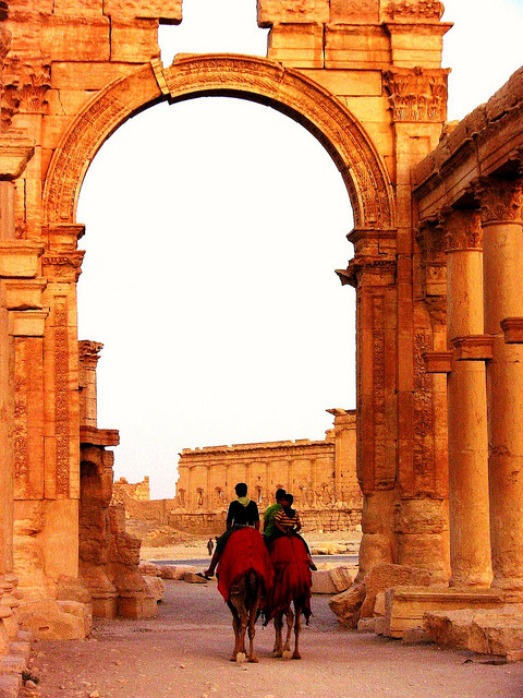 Camel riders crossing under the Arch of Hadrian in Palmyra, Syria